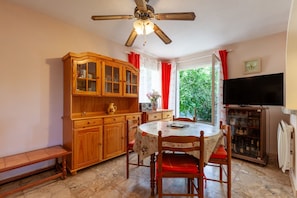 A dining area with a wooden cabinet, a round table with chairs, a ceiling fan, and a television.