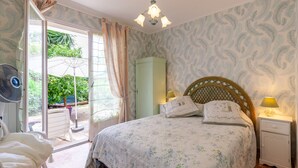 Une chambre à coucher avec un lit, une table de chevet, un ventilateur, une armoire et une vue sur la verdure à l’extérieur.