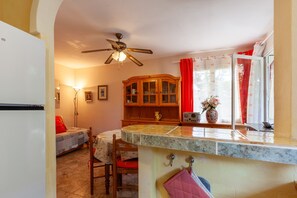 A kitchen with a marble countertop, wooden cabinets, a ceiling fan, and a dining area with a table and chairs.