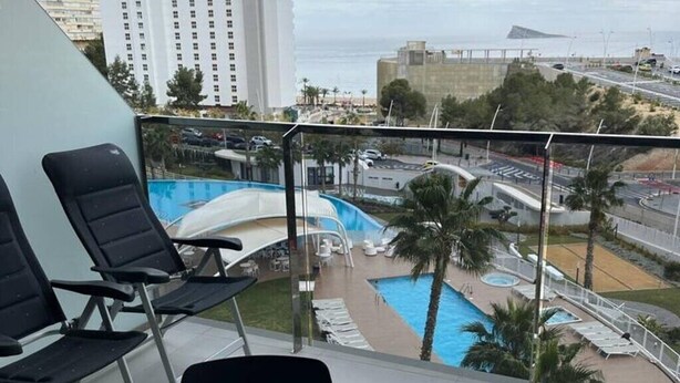 A balcony with a view of a swimming pool, lounge chairs, and a cityscape. - Apartment 'Sunset Waves' with Sea View, Wi-Fi and Air Conditioning (Benidorm)