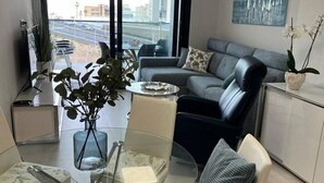 A modern living room with a glass coffee table, grey sofa, and a view of the cityscape through large windows. - Apartment 'Sunset Waves' with Sea View, Wi-Fi and Air Conditioning (Benidorm)