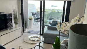A modern living room with a TV, seating, a small table, and a balcony with chairs. - Apartment 'Sunset Waves' with Sea View, Wi-Fi and Air Conditioning (Benidorm)