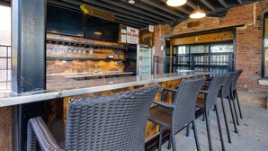 Un área de bar al aire libre con sillas de mimbre, una barra con vasos y un letrero que dice 'NO GLASS'.
