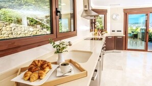 Eine Küche mit einer Platte Croissants und einer Tasse Kaffee, einer Steinwand und Blick auf das Meer.