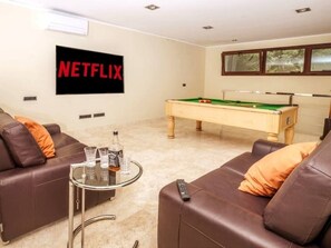 Ett vardagsrum med ett biljardbord, två lädersoffor, ett soffbord i glas och en väggmonterad TV.
