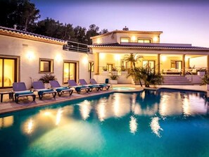 En vy över ett modernt hus med pool, solstolar och en täckt uteplats, sett från poolområdet.
