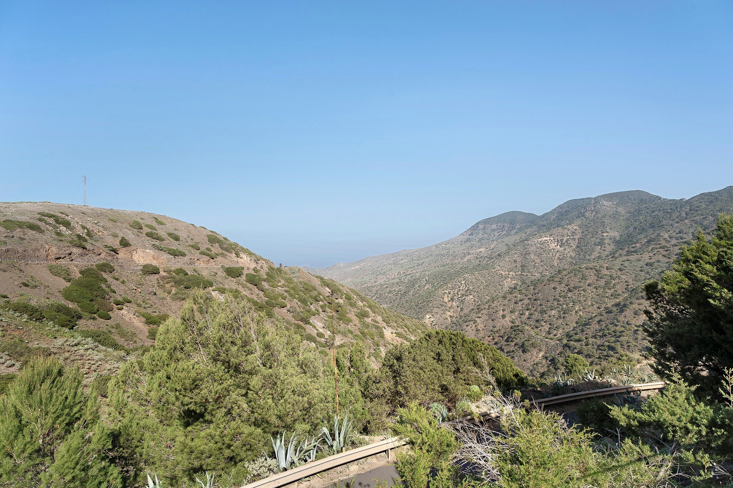 Eine gebirgige Landschaft mit blauem Himmel, einer Stromleitung und dichter Vegetation.