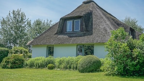 Une petite maison au toit de chaume, dotée de deux fenêtres et d’un jardin bien entretenu.