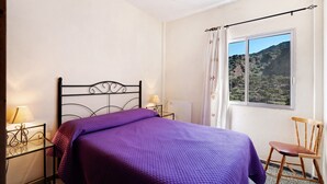 Une chambre à coucher avec un lit, une chaise, une fenêtre donnant sur un beau paysage et une lampe sur une table de chevet.