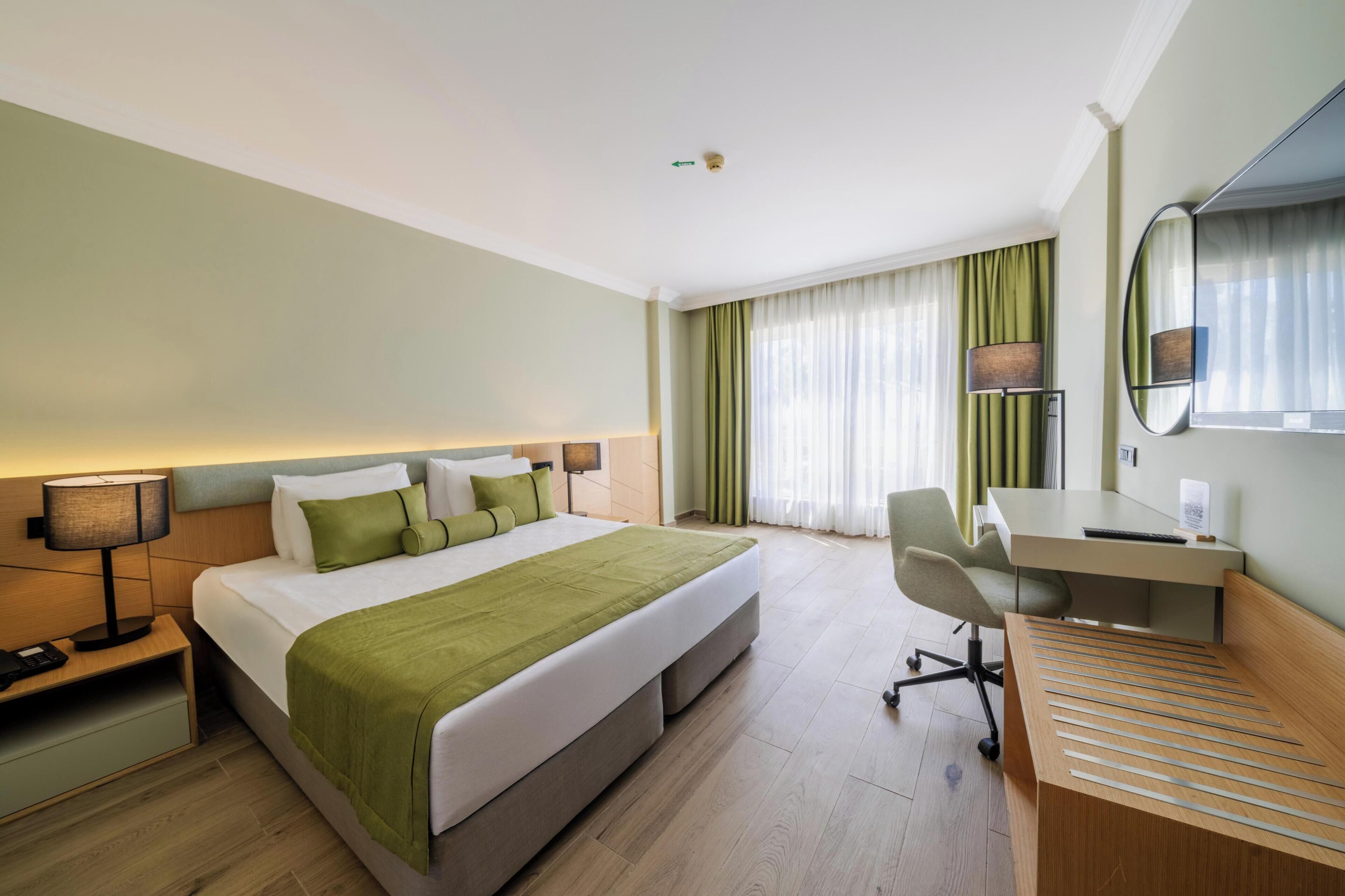 A hotel room with a bed, desk, chair, lamp, and curtains.