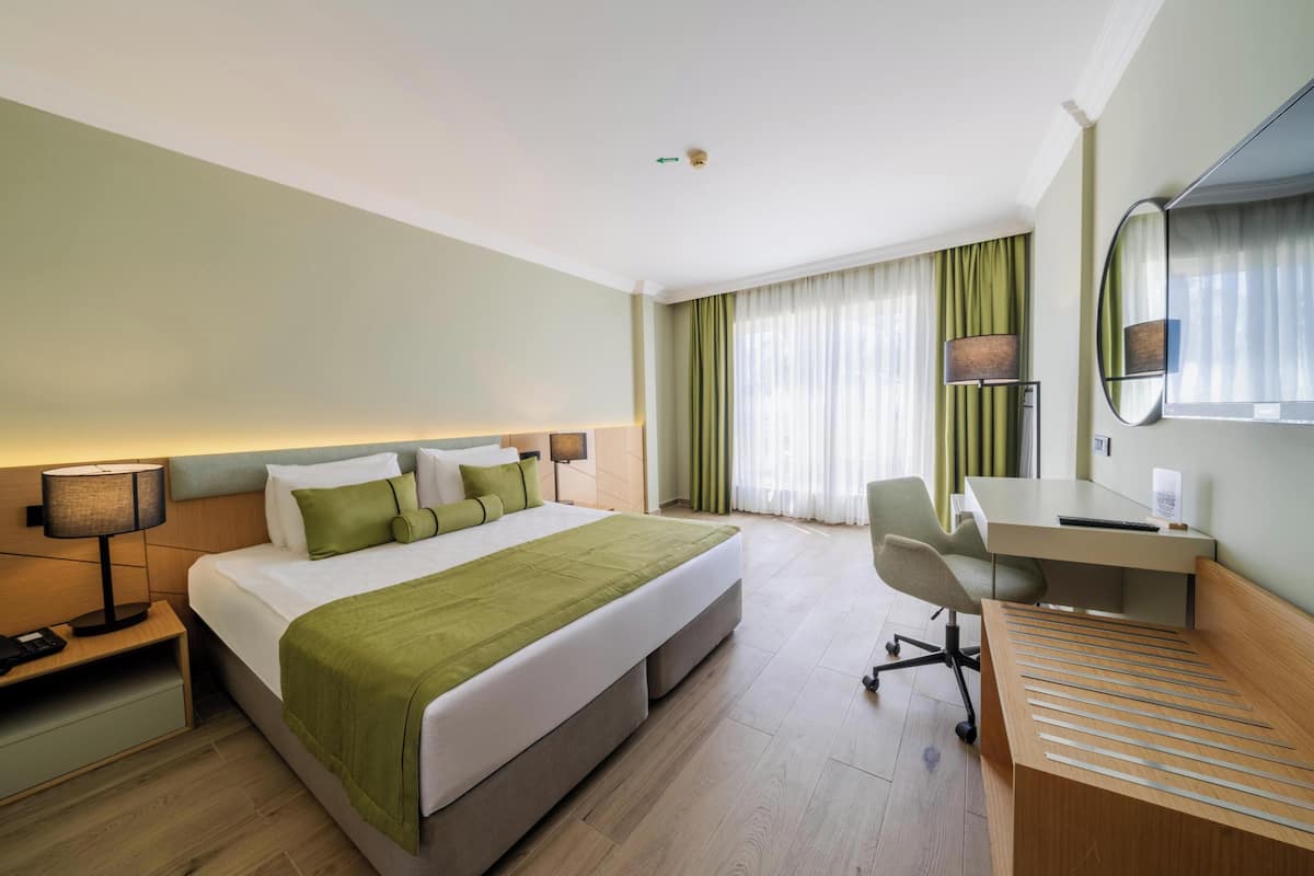 A hotel room with a bed, desk, chair, lamp, and curtains.