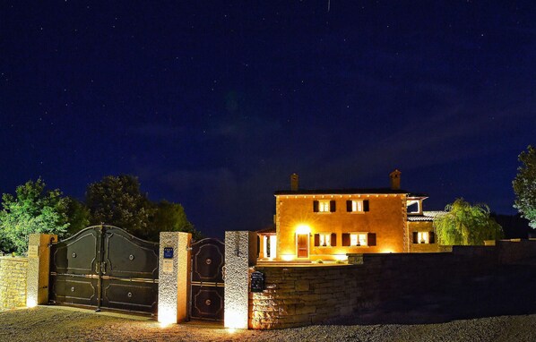 A two-story building with a stone wall and a large gate, illuminated by exterior lights.