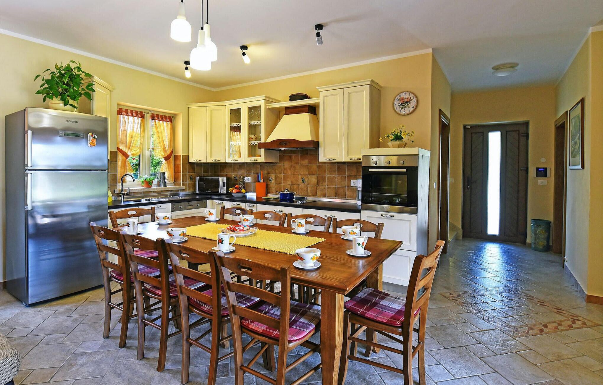 A kitchen with a dining table set for four, a refrigerator, a microwave, and an oven.