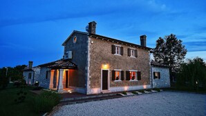 Une maison en pierre à deux étages, avec une allée en gravier et une pelouse bien entretenue.