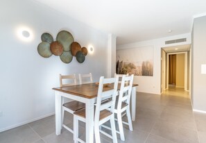 A dining area with a wooden table and white chairs, a wall-mounted decorative piece, and a hallway leading to another room. - Apartment 'Apartamento Ponent 3' with Private Terrace, Wi-Fi and Air Conditioning (Cala Ratjada)
