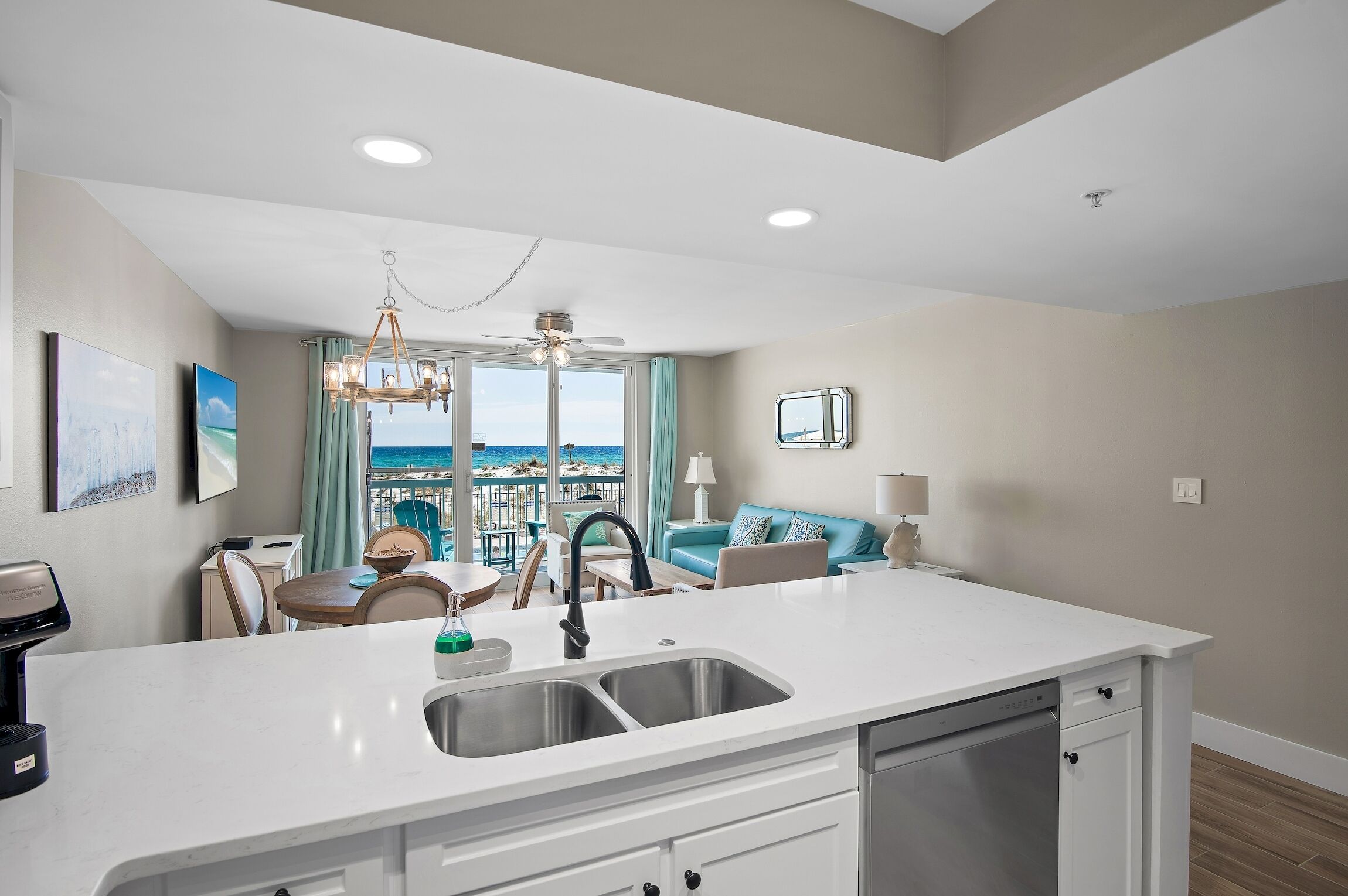 A modern kitchen with a central island, a dining area with a view, and a living space with a sofa and a lamp.