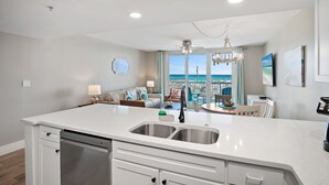 A modern kitchen with a large island, a dining area with a view, and a living space with a sofa and a TV. - Renovated beachfront condo, spectacular Gulf views (Destin)