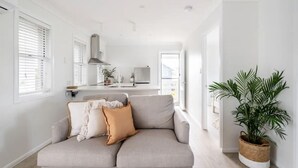 Ett modernt vardagsrum med en grå soffa, en krukväxt och ett kök i bakgrunden.