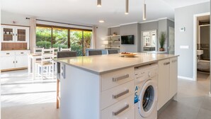 A modern kitchen with a built-in washing machine, a dining area with a table and chairs, and a large window offering a view of greenery. - Apartment 'Apartamento Ponent 6' with Private Terrace, Wi-Fi and Air Conditioning (Cala Ratjada)