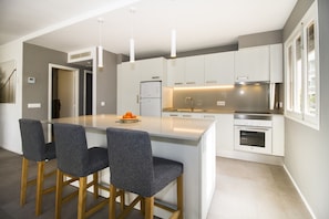 Una cucina moderna con isola centrale, sgabelli da bar, frigorifero, forno e illuminazione a sospensione.