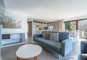 En moderne stue med sofa, rundt sofabord og et køkken i baggrunden.