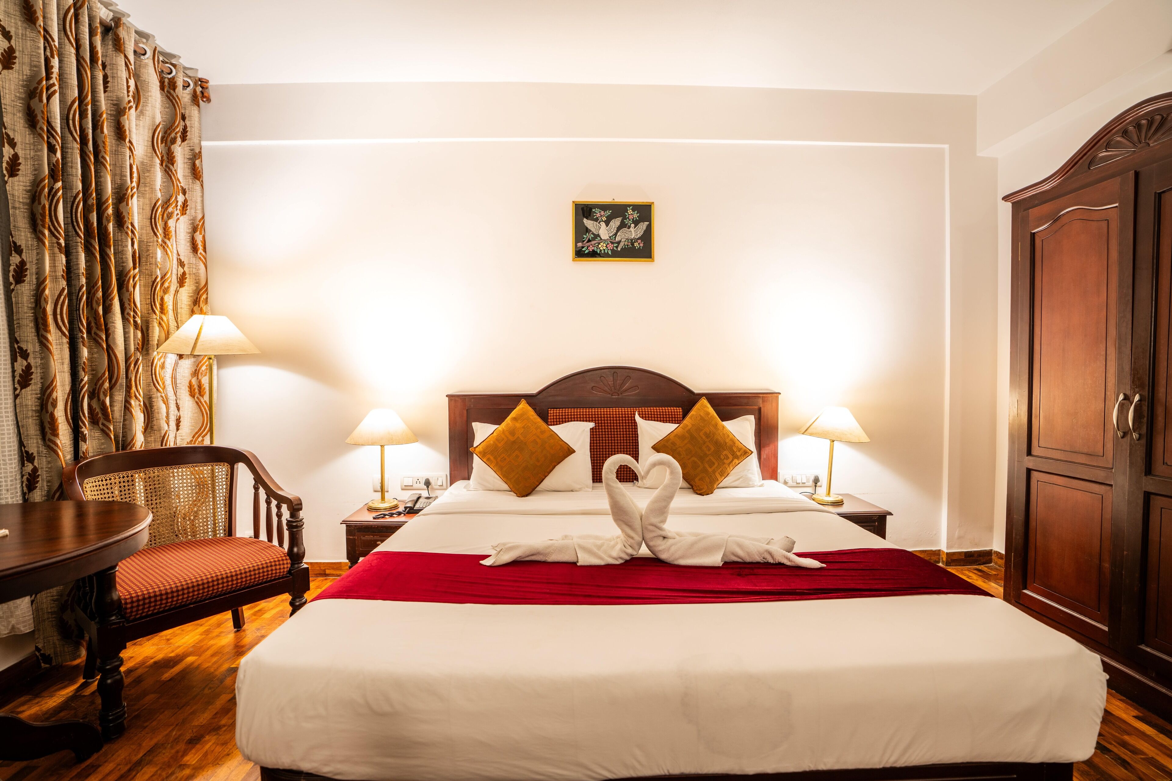 A hotel room with a large bed, two nightstands, a wooden wardrobe, a dining table, and a chair.