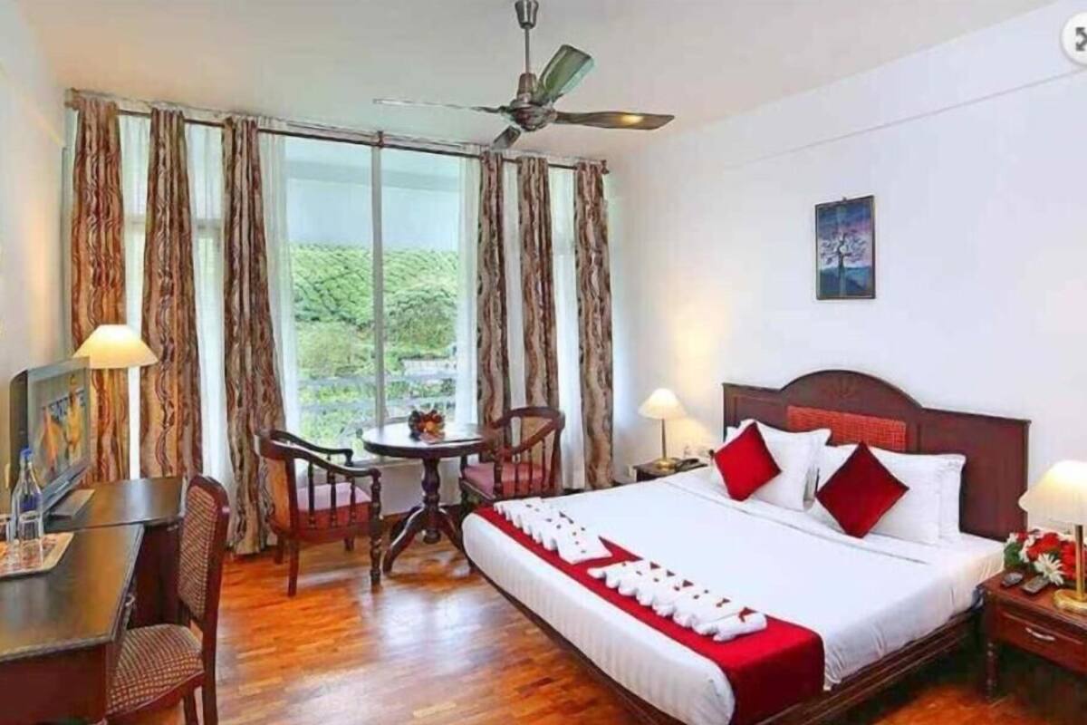 A hotel room with a bed, desk, chair, and a view of greenery outside.
