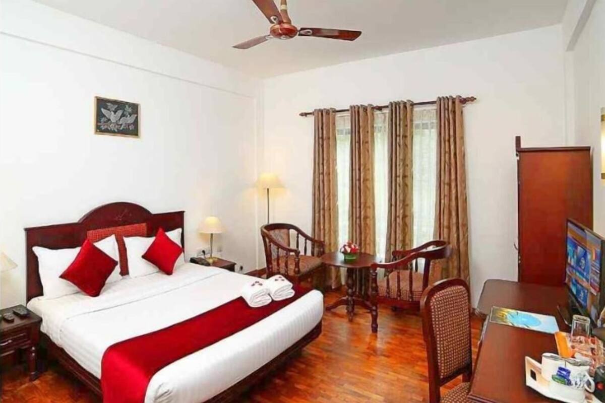 A hotel room with a bed, a desk, a chair, a ceiling fan, and a window with curtains.