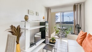 A modern living room with a flat-screen TV, a sofa with orange cushions, a small table, and a potted plant. - Apartment 'Les Embruns' with Sea View, Private Terrace and Balcony (Empuriabrava)