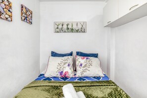 Un llit amb un estovat estampat, dos almoiners amb motius florals i una manta verda.