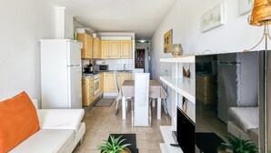 A modern kitchen with white cabinets, a dining area with a white table and chairs, and a living area with a white sofa and orange pillow. - Apartment 'Les Embruns' with Sea View, Private Terrace and Balcony (Empuriabrava)