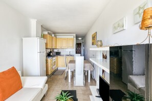 Una cocina moderna con armarios blancos, un comedor con mesa y sillas blancas, y una sala de estar con sofá blanco y almohada naranja.