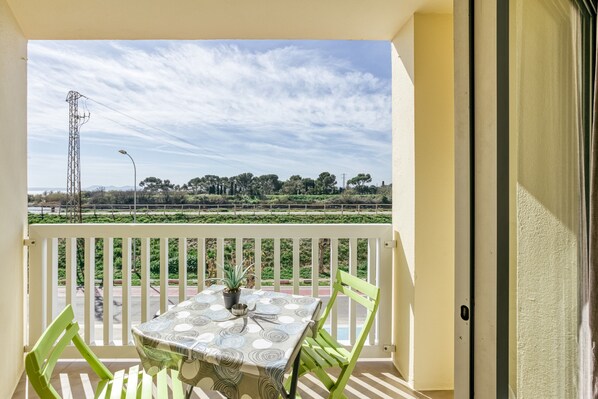 Un balcon avec une table et des chaises, un pot de fleurs et une vue sur un champ verdoyant et des arbres au loin.