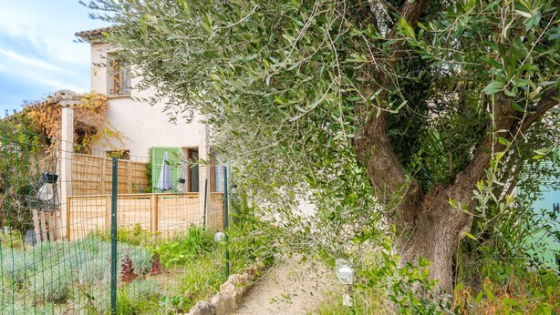 A rustic house with a dirt path leading to a wooden gate, surrounded by greenery and a fence. - Apartment 'Vallon Des Prés' with Private Terrace, Shared Garden and Wi-Fi (Villeneuve-Loubet)