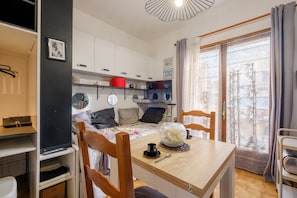 Una habitación compacta con una cama, un escritorio, una mesa con un objeto de vidrio decorativo, una silla y vistas a través de una ventana con cortinas.