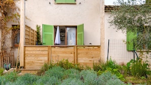 A rustic building with a wooden fence, a window with green shutters, and a garden in front. - Apartment 'Vallon Des Prés' with Private Terrace, Shared Garden and Wi-Fi (Villeneuve-Loubet)