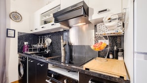 A compact kitchen with a built-in washer, a stainless steel range hood, and a fruit bowl on the countertop. - Apartment 'Vallon Des Prés' with Private Terrace, Shared Garden and Wi-Fi (Villeneuve-Loubet)
