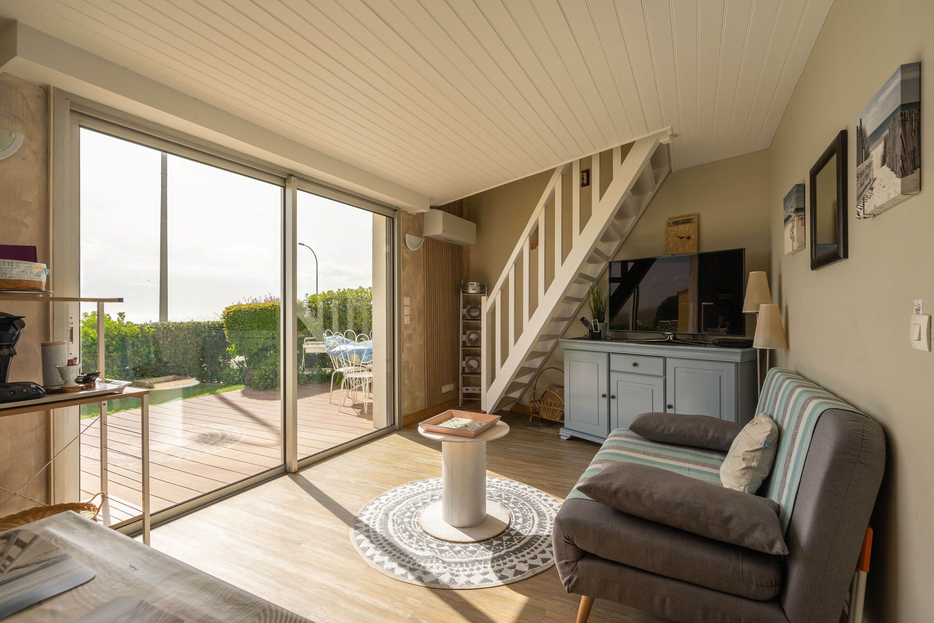 A spacious living area with a large sliding glass door leading to a deck, a sofa, a small round table, and a staircase.