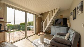 A spacious living area with a large sliding glass door leading to a deck, a sofa, a small round table, and a staircase.