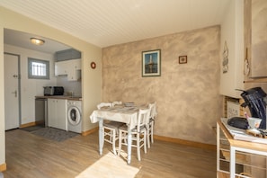 A compact kitchen with a washing machine, a dining table with chairs, and a coffee machine.