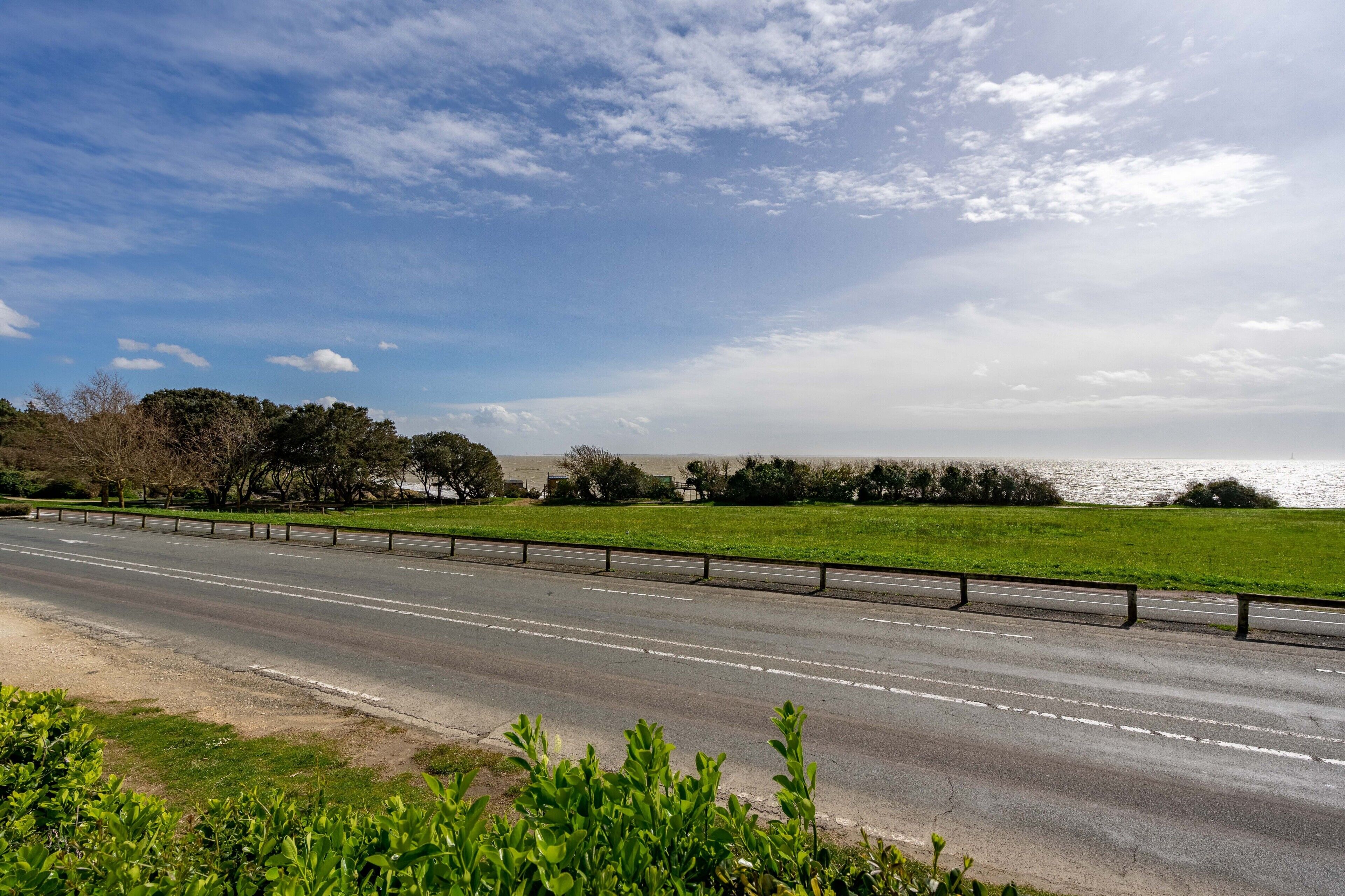 Une autoroute bordée de glissières de sécurité, avec de l’herbe verte et des arbres en arrière-plan.