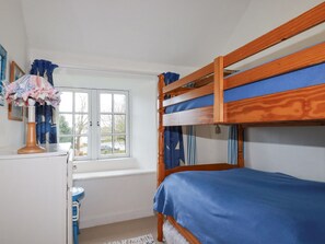 Une chambre avec un lit superposé, une fenêtre, un bureau avec une lampe et des rideaux.