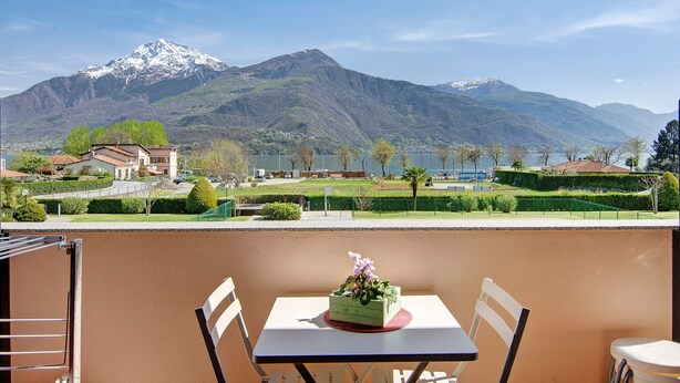 Un balcon avec une table et des chaises, d’où l’on a vue sur une montagne et un lac.