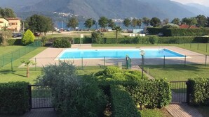 Une piscine rectangulaire entourée d’une clôture, avec un chemin pavé et une végétation luxuriante.