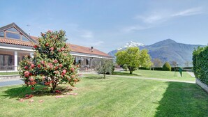 Une maison avec un toit recouvert de tuiles rouges, une pelouse et une montagne en arrière-plan.