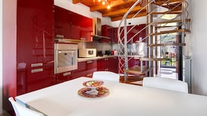 Une cuisine moderne avec des meubles rouges, une table à manger blanche et un escalier en colimaçon.