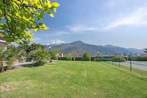 Un prato curato, un campo da tennis e una montagna sullo sfondo con cime innevate.