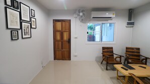 A room with a wooden door, framed artwork on the wall, a fan, and a table with chairs. - No.9 hostel kanchanaburi (Kanchanaburi)