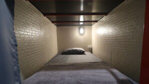 A narrow, brick-walled room with a single bed, a light fixture on the ceiling, and a wall socket. - No.9 hostel kanchanaburi (Kanchanaburi)