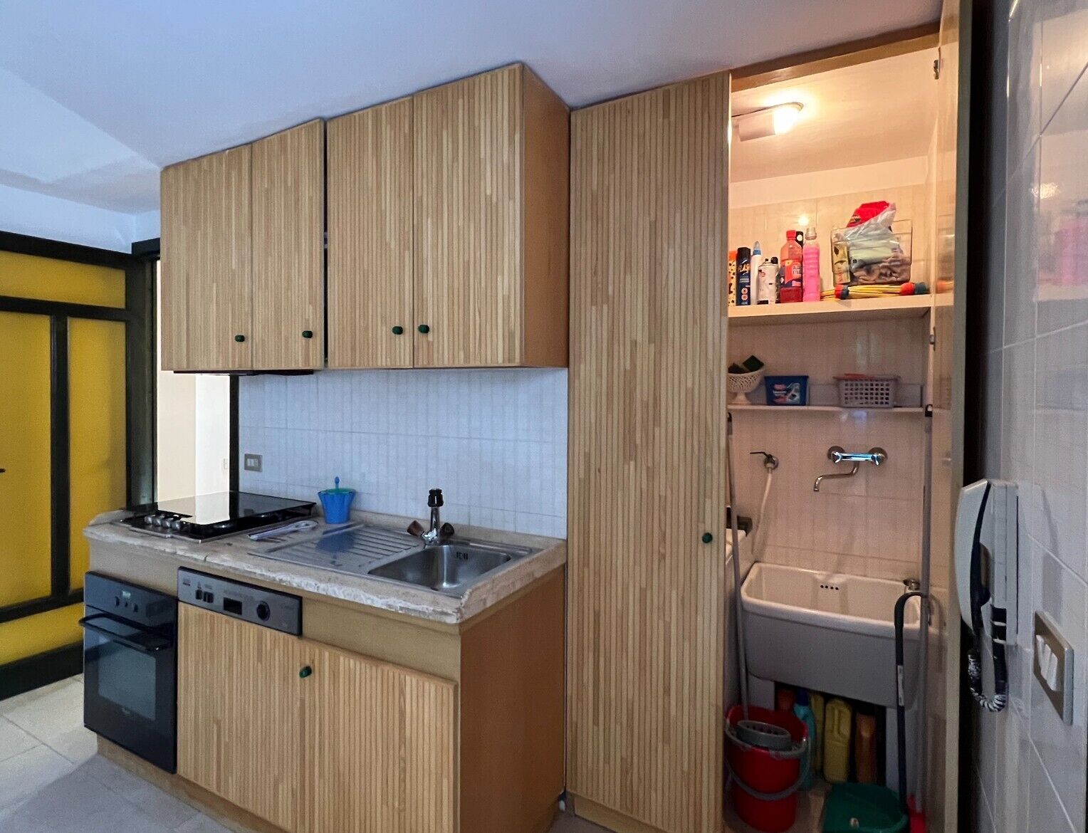 Una cucina compatta con mobili in legno, piano cottura integrato, lavastoviglie e lavello.